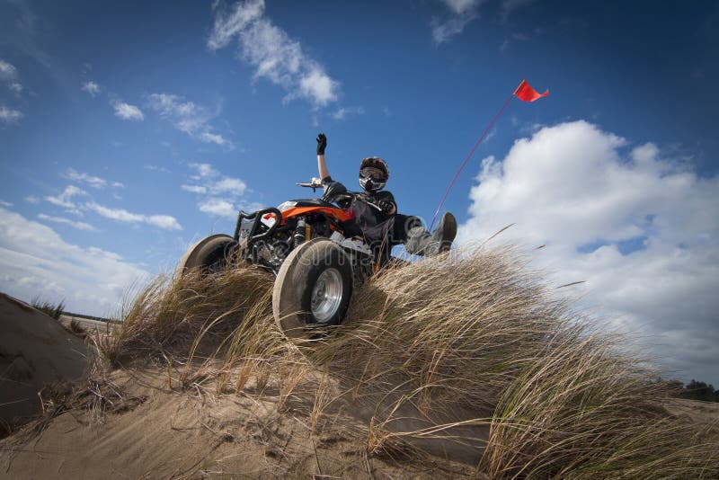 Male teen on ATV coming over grassy sand hill. Male teen on ATV coming over grassy sand hill