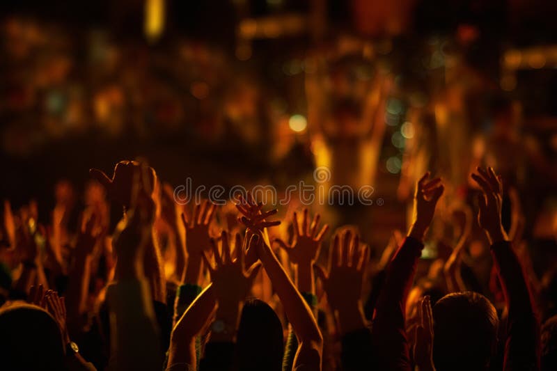 Audience with hands raised at a music festival and lights streaming down from above the stage.