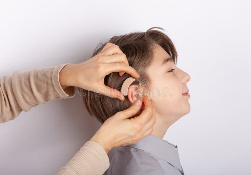 Audiologist fitting hearing aid on a smilling young boy
