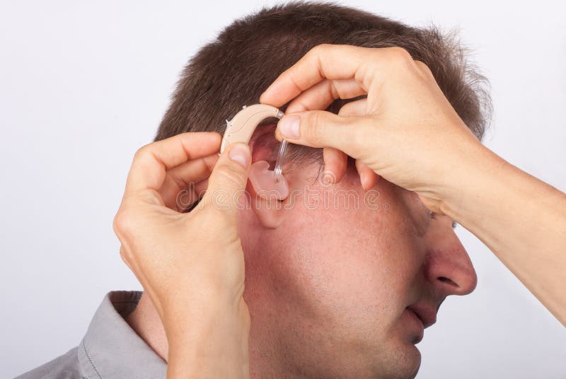 Audiologist fitting a man patient with hearing aid