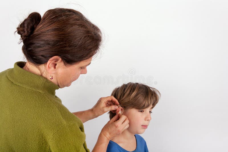 Audiologist woman fitting a young boy with a hearing aid