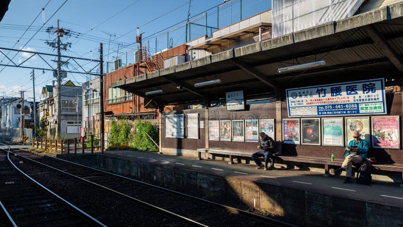 Auf der Bank sitzende Touristen warten nächsten Zug am Bahnhof Ryoanji lizenzfreie stockbilder Auf der Bank sitzende Touristen warten nächsten Zug am Bahnhof Ryoanji lizenzfreie stockbilder
