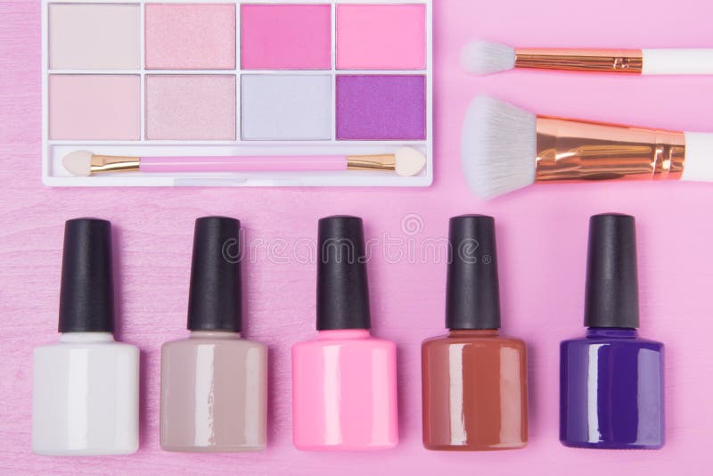 Auf einem rosa Hintergrund sind mehrfarbige Nagellacke in der unteren Reihe, Lidschatten und Bürsten sind auf Oberseite stockbild Auf einem rosa Hintergrund sind mehrfarbige Nagellacke in der unteren Reihe, Lidschatten und Bürsten sind auf Oberseite stockbild