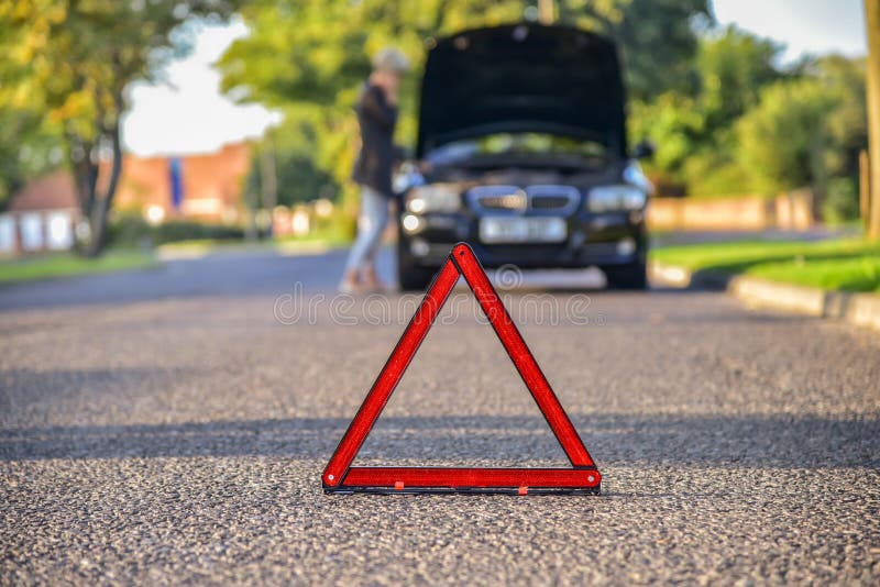 Broken down car with warning triangle, waiting for assistance to arrive (shallow depth of field, the focus is on the triangle, the car is left out of focus). Broken down car with warning triangle, waiting for assistance to arrive (shallow depth of field, the focus is on the triangle, the car is left out of focus).