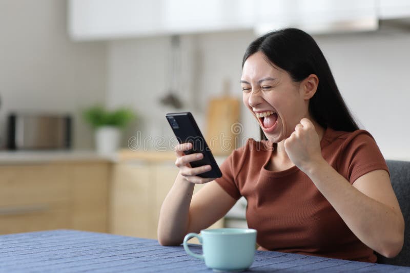 Aufgeregte asiatische Frau telefonisch in der Küche stockfoto
