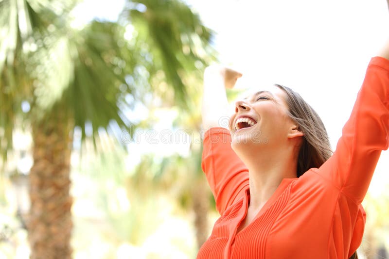 Portrait of an excited woman with eyes closed raising arms skyward outdoors with palm trees in the background. Portrait of an excited woman with eyes closed raising arms skyward outdoors with palm trees in the background