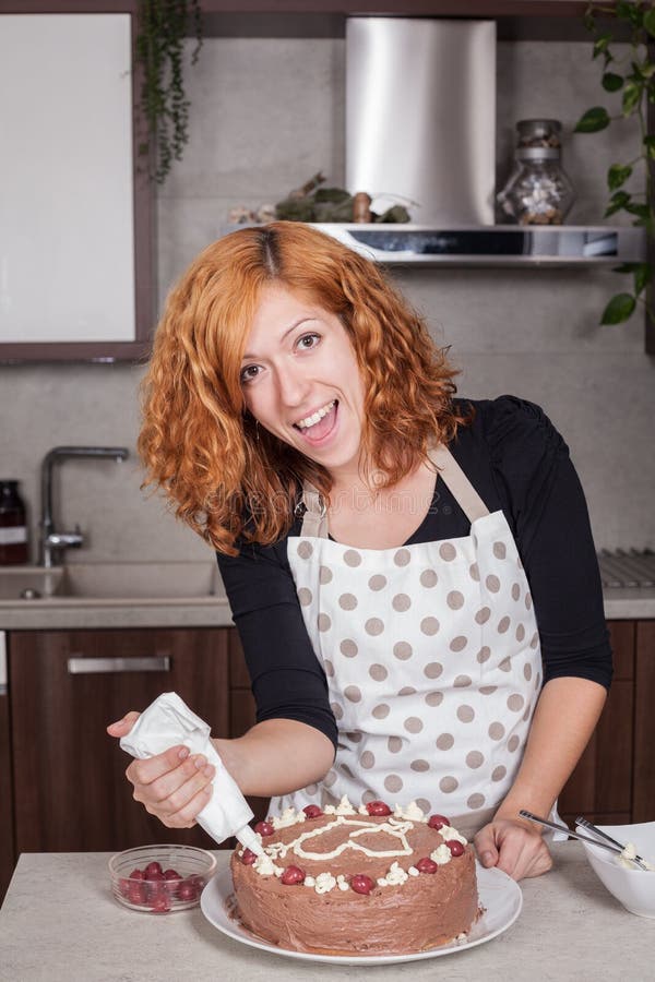 Aufgeregte Frau, die zu Hause Kuchen verziert stockfotografie Aufgeregte Frau, die zu Hause Kuchen verziert stockfotografie