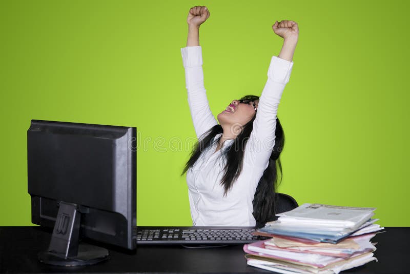 Excited business woman celebrating success by lifting her hands while working with a computer. Shot with green screen. Excited business woman celebrating success by lifting her hands while working with a computer. Shot with green screen