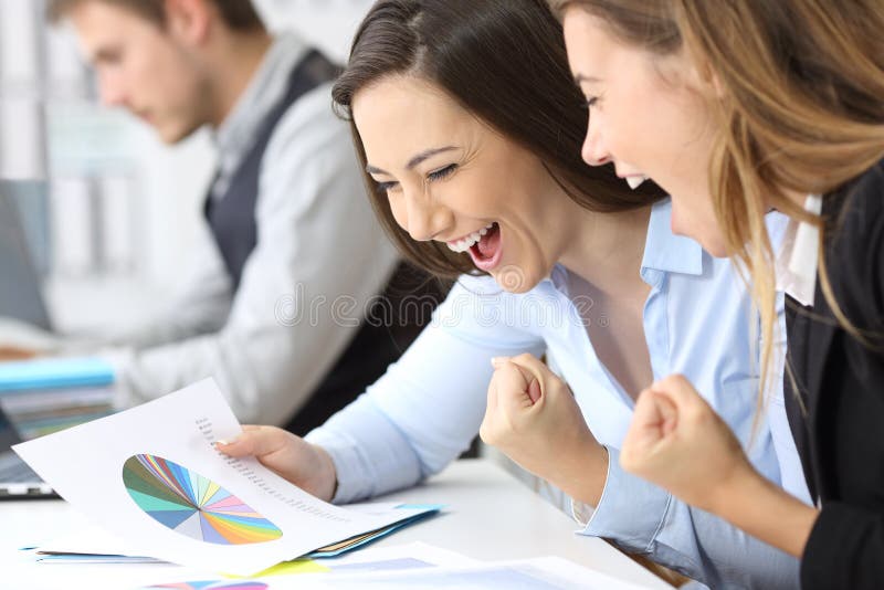 Two excited businesswomen celebrating success reading growth graphs at office. Two excited businesswomen celebrating success reading growth graphs at office