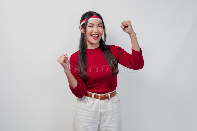 Aufgeregte junge Asiatin in einem roten Hemd und weiße Hosen heben ihre Hände. stockfoto