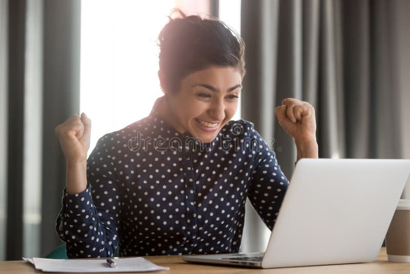 Excited young indian student receiving notification about hiring to work or unexpected good news. Happy successful female employee celebrating victory win achievement or job promoting. Excited young indian student receiving notification about hiring to work or unexpected good news. Happy successful female employee celebrating victory win achievement or job promoting.