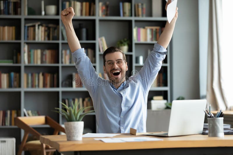 Excited overjoyed man received good news in letter, job promotion or great exam result, happy businessman or student celebrate success, shouting, raising hands, sitting at workplace with laptop. Excited overjoyed man received good news in letter, job promotion or great exam result, happy businessman or student celebrate success, shouting, raising hands, sitting at workplace with laptop
