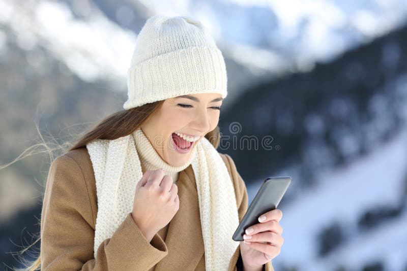 Excited girl checking online news in winter in a snowy mountain. Excited girl checking online news in winter in a snowy mountain