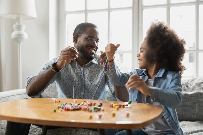 Aufgeregtes schwarzes Mädchen und glücklicher Papa, die bunte Holzperlen aufreiht lizenzfreies stockfoto