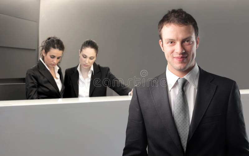 Smiling businessman with two receptionists on the background. Smiling businessman with two receptionists on the background