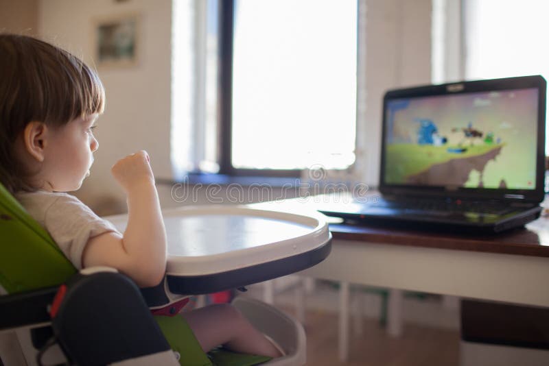 Aufpassende Karikaturen eines kleinen blonden Jungen auf dem Laptop beim Sitzen auf Kind-` s Stuhl stockbild Aufpassende Karikaturen eines kleinen blonden Jungen auf dem Laptop beim Sitzen auf Kind-` s Stuhl stockbild