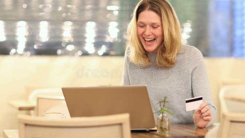 Aufregte Frau, die online in einem Coffee Shop einkauft