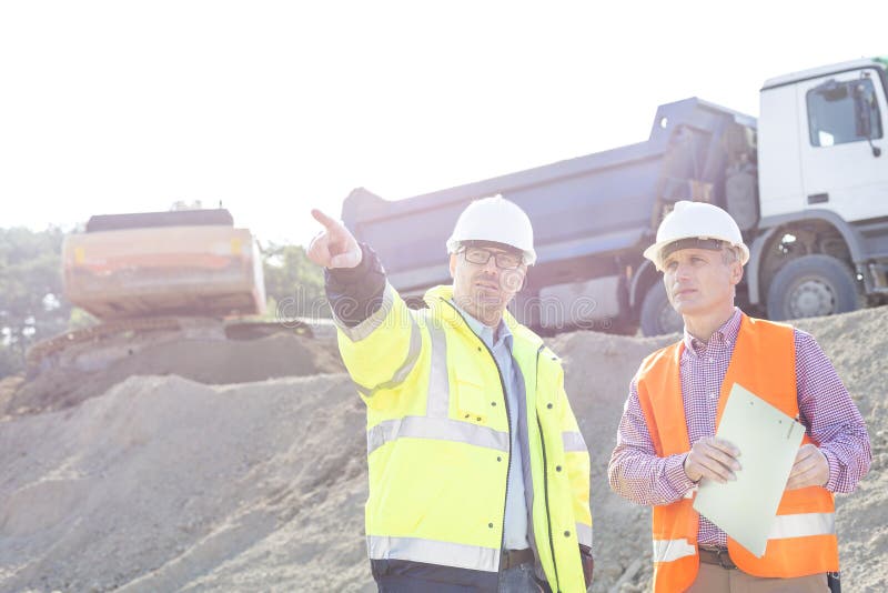 Aufsichtskraft, die dem Kollegen etwas bei der Diskussion an der Baustelle zeigt lizenzfreies stockbild Aufsichtskraft, die dem Kollegen etwas bei der Diskussion an der Baustelle zeigt lizenzfreies stockbild