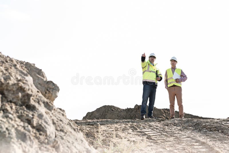 Aufsichtskraft, die mit Kollegen an der Baustelle gegen klaren Himmel sich bespricht lizenzfreie stockfotos Aufsichtskraft, die mit Kollegen an der Baustelle gegen klaren Himmel sich bespricht lizenzfreie stockfotos