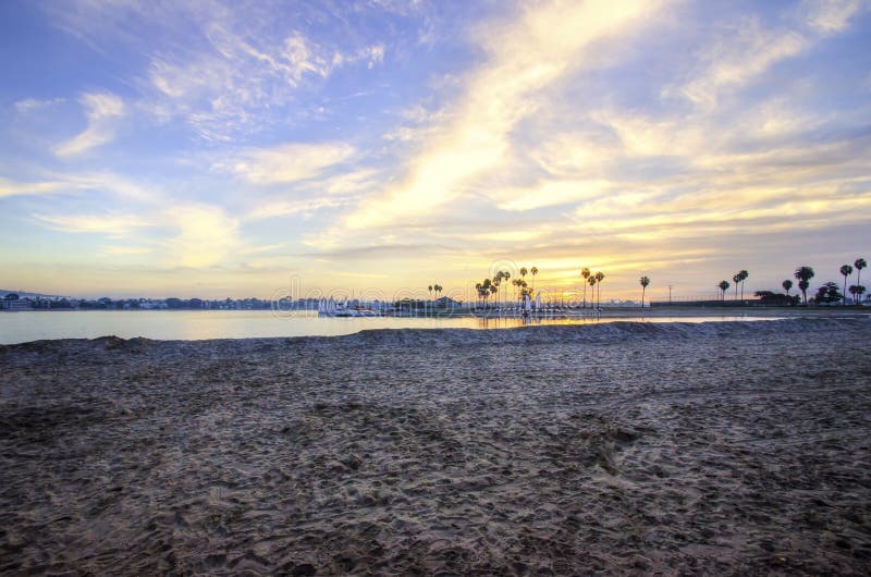 The sunrise over Sail bay in Mission Bay over the Pacific beach in San Diego, California in the United States of America. A view of the sandy beach, palm trees and beautiful saltwater bay at sunset. The sunrise over Sail bay in Mission Bay over the Pacific beach in San Diego, California in the United States of America. A view of the sandy beach, palm trees and beautiful saltwater bay at sunset.