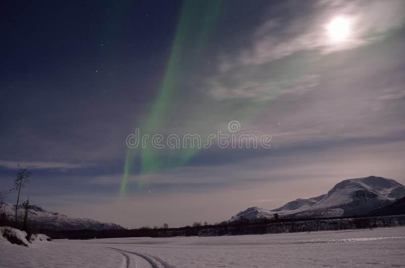 Aurora borealis, northern light over a frozen snowy river bed with full moon and majestic mountain stock photography Aurora borealis, northern light over a frozen snowy river bed with full moon and majestic mountain stock photography