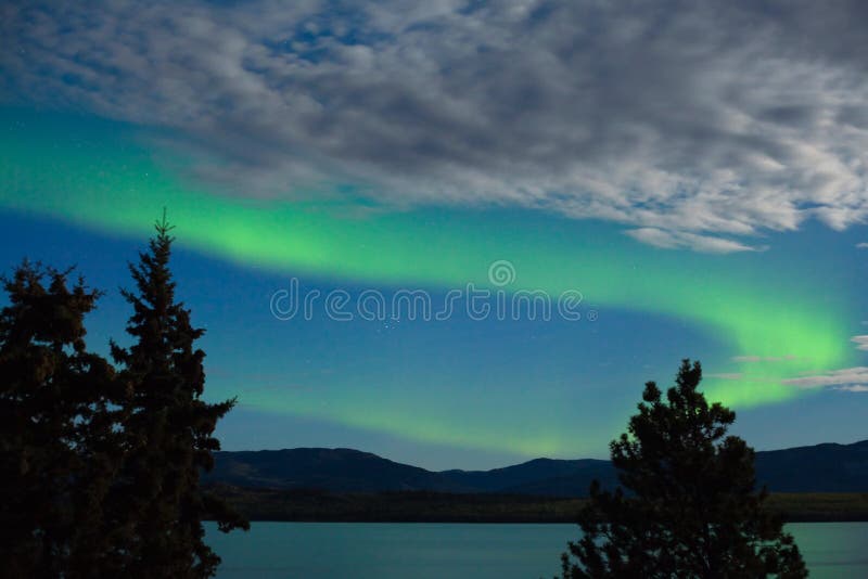 Aurora borealis (Northern lights) display. Intense Aurora borealis showing between clouds during moon lit night over Lake Laberge, Yukon Territory, Canada stock photo Aurora borealis (Northern lights) display. Intense Aurora borealis showing between clouds during moon lit night over Lake Laberge, Yukon Territory, Canada stock photo