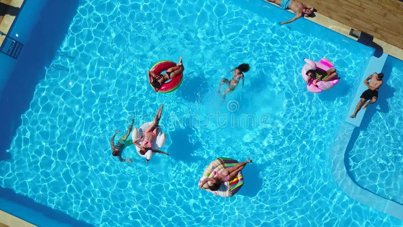 Aus der Luft. Freunde, die im Swimmingpool mit aufblasbarer Flamingoschwanmatratze kühlen. glückliche Jugendliche baden auf dem Sc