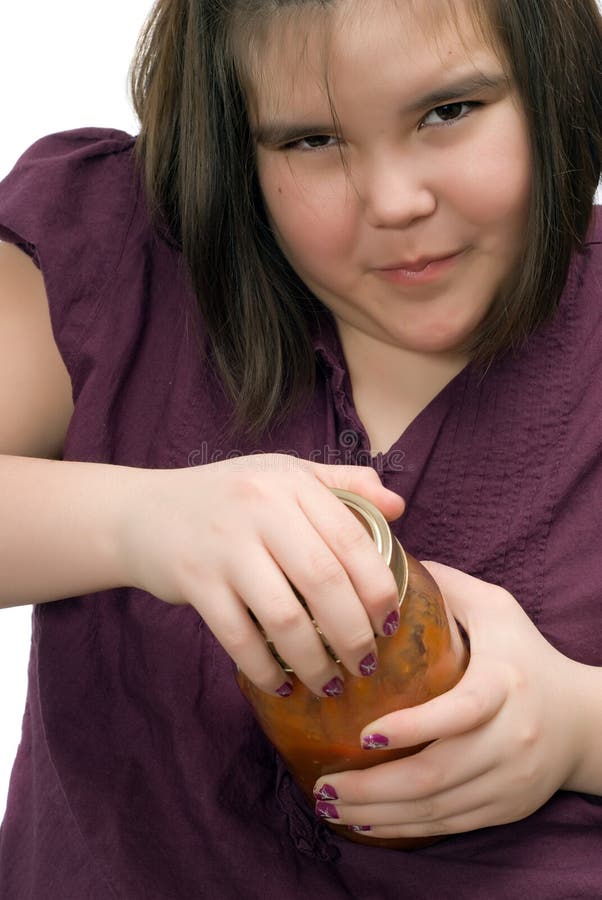 Closeup of a young girl being persistent and trying to open a glass jar of tomato salsa. Closeup of a young girl being persistent and trying to open a glass jar of tomato salsa