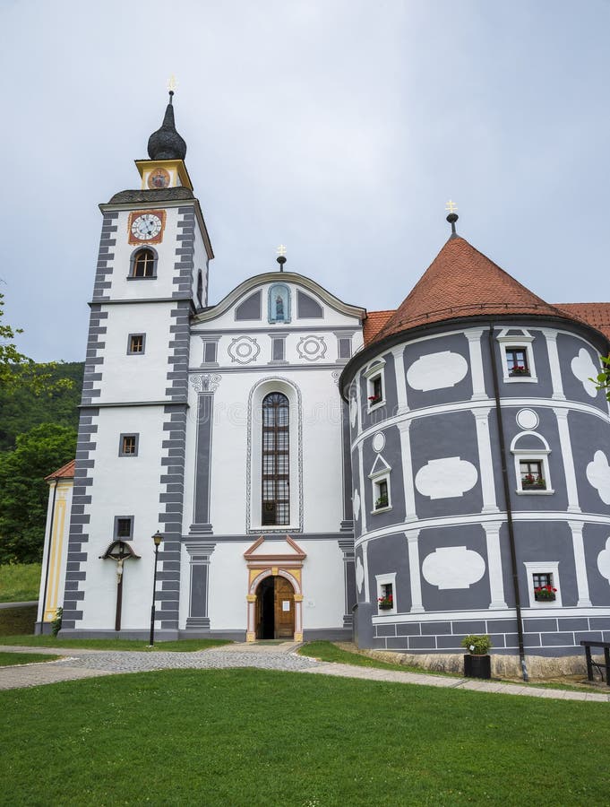 Aussicht auf das Kloster Olimje mit Uhrturm und Haustür Podcetrtek Slowenien 20 Juni 2019. Eine charmante historische Kirche besticht durch ihre geschmückte Architektur, zu der ein Uhrturm und zylindrische Bauelemente gehören, die sich an einem ruhigen grünen Rasen unter einem sanften bewölkten Himmel anschließen und Ruhe und Ruhe ausstrahlen