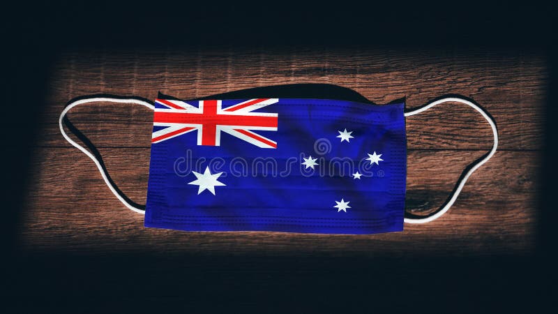 Australia National Flag at medical, surgical, protection mask on black wooden background. Coronavirus Covidâ€“19, Prevent infection, illness or flu concept photo. State of Emergency, Lockdown