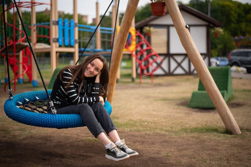 Authentic portrait of a young smiling woman on a hanging swing, the concept of freedom, day off, remember childhood.