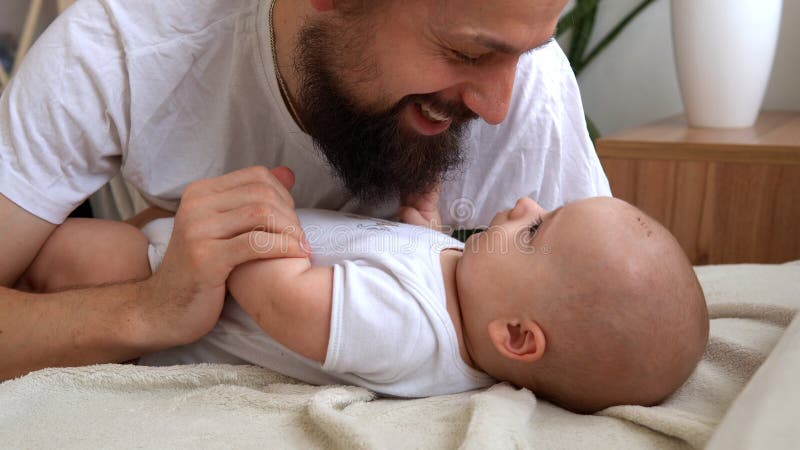 Authentic Young Bearded Man Holding Newborn Baby. Dad And Child Son On Bed. Close-up Portrait of Smiling Family With