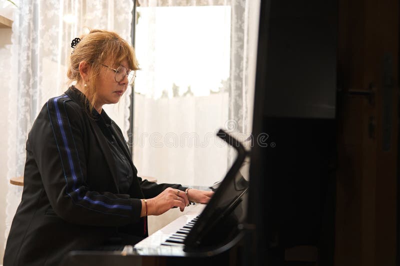 Authentique femme asiatique mature en tenue décontractée noire jouer du piano et chanter cours de piano à la maison images stock