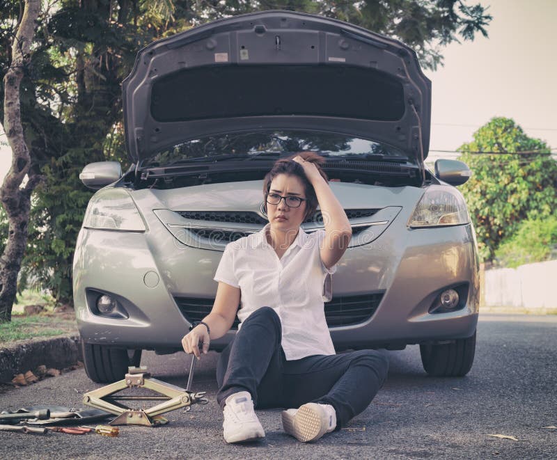 Woman sitting on ground and using mobile phone near her car broken down on the road side. Woman sitting on ground and using mobile phone near her car broken down on the road side.