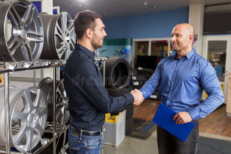 Business, partnership and people concept - male customer and salesman shaking hands at car repair service or auto store. Business, partnership and people concept - male customer and salesman shaking hands at car repair service or auto store