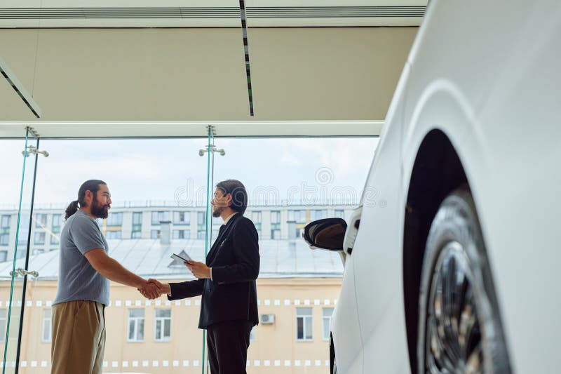 Auto Dealer Shaking Hands with Buyer in Showroom at Dealership Center royalty free stock images