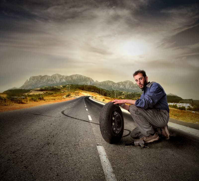 Ritratto di meccanico auto con una ruota su una strada di campagna.