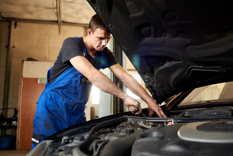 Auto mechanic in dirty work uniform repairs car in garage