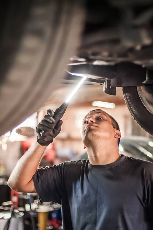 Auto Mechanic Repairer Checking Condition Under Car on Vehicle Lift