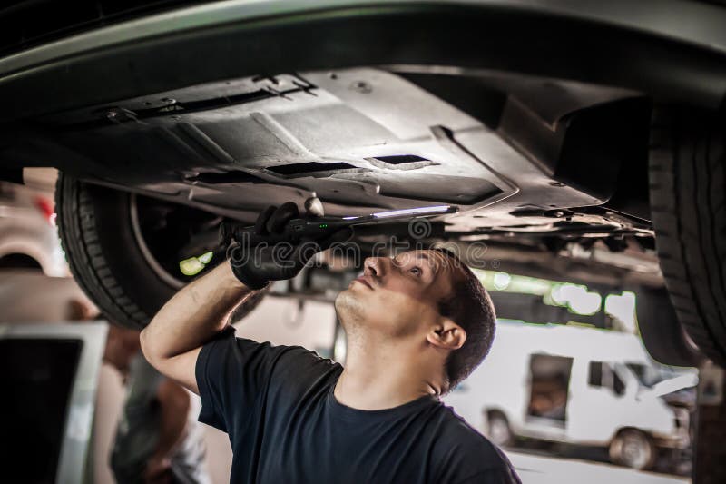 Auto Mechanic Repairer Checking Condition Under Car on Vehicle Lift