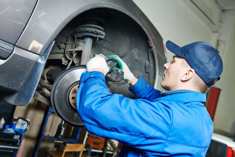 Car mechanic worker repairing brakes of lifted automobile at auto repair garage shop station. Car mechanic worker repairing brakes of lifted automobile at auto repair garage shop station