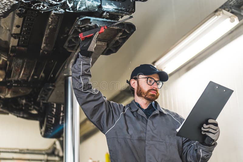 An Auto Serviceman Looking into the Papers while Chassis Inspection in