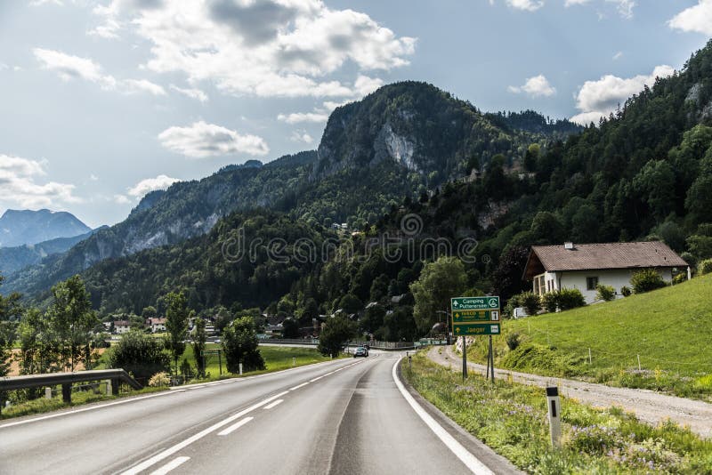 Autobahn or highway with a bridge in the mountains with clear marking surrounded by vibrant green trees under blue sky. Mountain