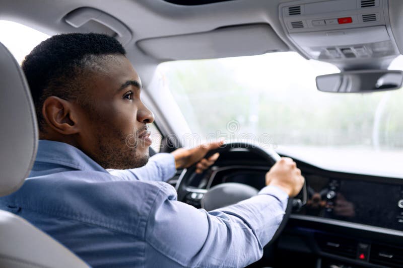 Autofahren. Junger schwarzer Mann sitzt in einem neuen Auto und hält Lenkrad im Inneren und schaut nach hinten Schuss. stockfoto