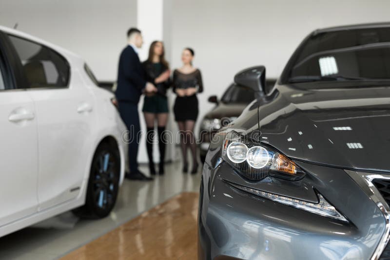 Auto business, car sales - a couple of friends of girls with a car dealer choose a car in a car dealership. Auto business, car sales - a couple of friends of girls with a car dealer choose a car in a car dealership.