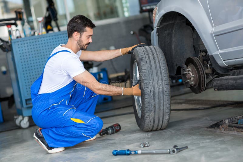 Automechaniker, der Rad eines Autos abmontiert stockbild Automechaniker, der Rad eines Autos abmontiert stockbild