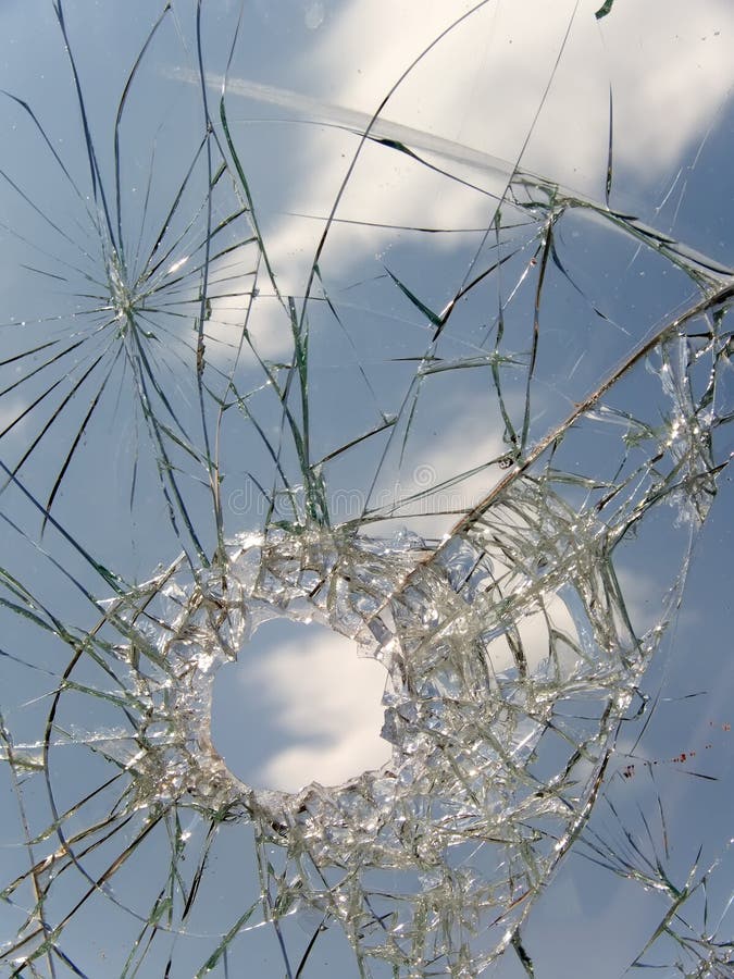 Hole, cracks splinters in the broken automobile glass against the sky. Hole, cracks splinters in the broken automobile glass against the sky