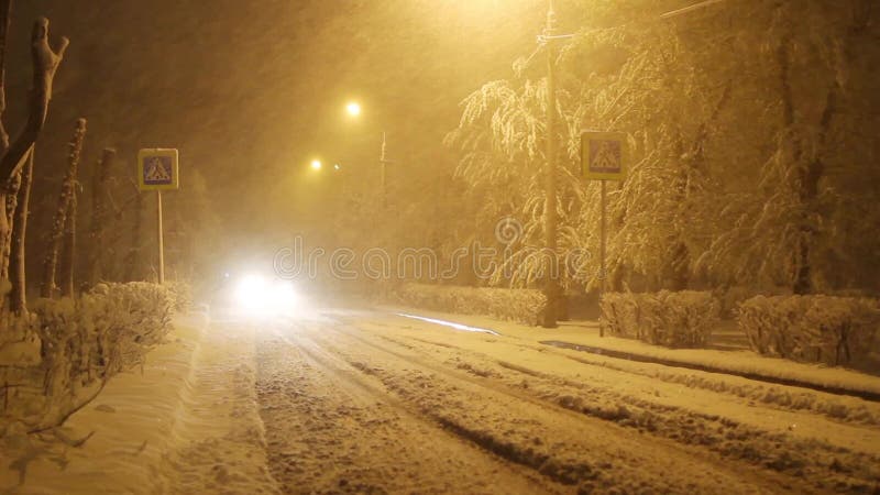 Automobile sulla strada di inverno nella bufera di neve, traffico su una via nevosa della città alla notte, segno del passaggio p