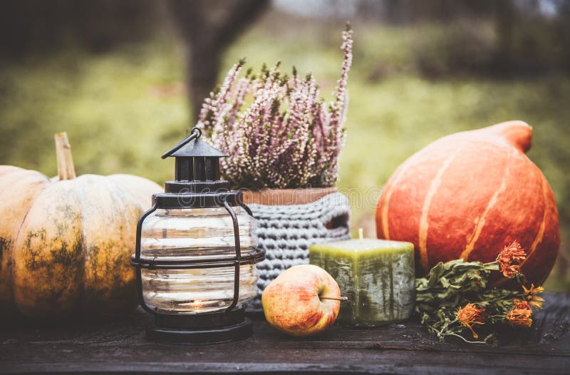 Autumn background with lantern, pumpkins, apple and heather flower in crochet pot outdoors in dark autumn day.