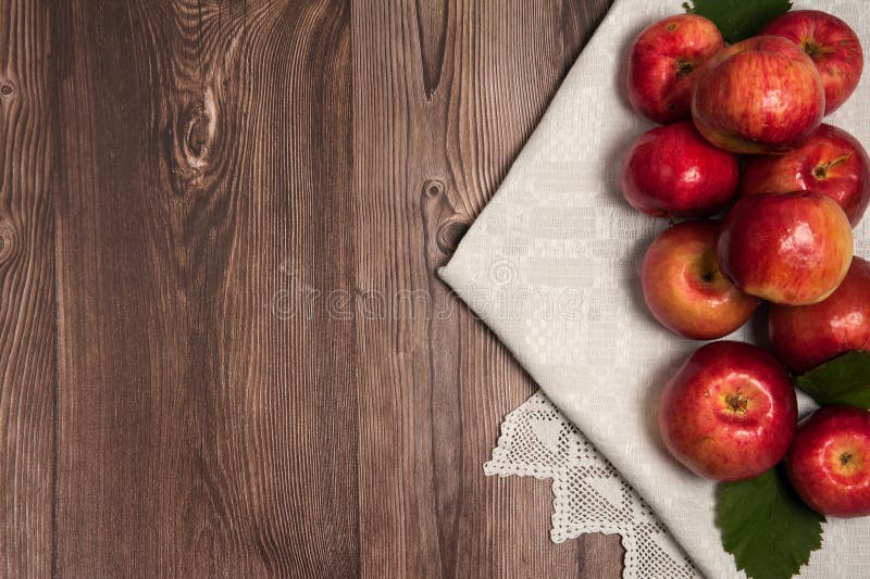 Red apples, green leaves, linen napkin with handmade lace on a wooden background. stock photos